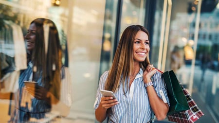 Frau mit Papiertüten und Smartphone beim Shopping vor einem Geschäft