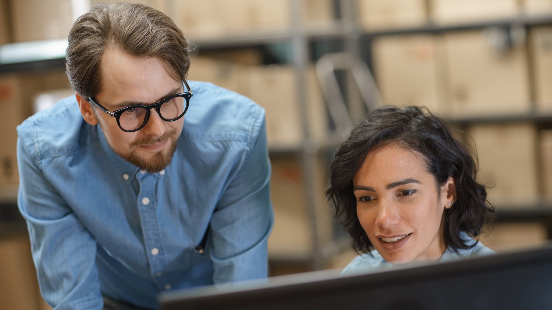 Male and Female Warehouse Inventory Managers Talking Using Personal Computer and Checking Stock