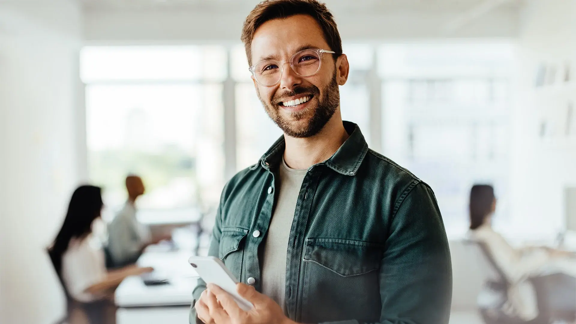 Ein Mann steht mit einem Smartphone in der Hand im Büro